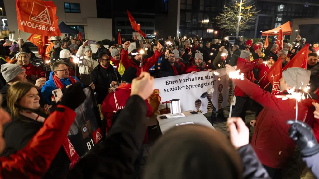 At Volkswagen's Wolfsburg headquarters in Germany, participants at an IG Metall union rally hold sparklers and a banner that reads: "Your plans are social explosives," on November 30, 2024. Michael Matthey/picture-alliance/dpa/AP