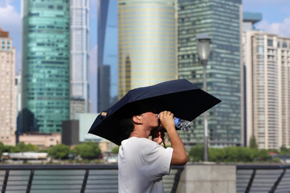 A man drinks from under an umbrella during a red alert heatwave in Shanghai in August 2024.Nicoco Chan / Reuters