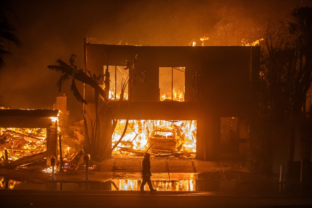 A firefighter watches flames from the Palisades Fire burn homes on Pacific Coast Highway in Los Angeles on Wednesday.Apu Gomes / Getty Images