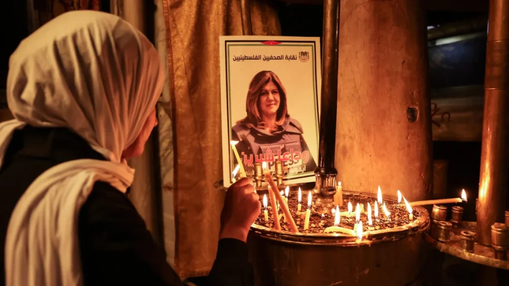 A woman lights a candle in front of a poster depicting veteran Al-Jazeera journalist Shireen Abu Akleh, who was shot dead while covering an Israeli army raid in Jenin, at the the Church of the Nativity in the West Bank biblical city of Bethlehem on May 11, 2022. (Hazem Bader/AFP/Getty Images)