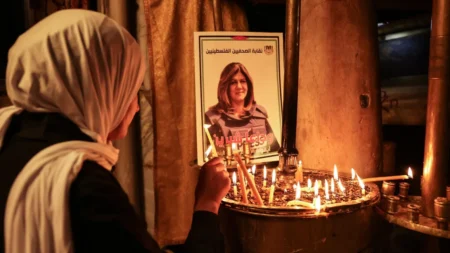 A woman lights a candle in front of a poster depicting veteran Al-Jazeera journalist Shireen Abu Akleh, who was shot dead while covering an Israeli army raid in Jenin, at the the Church of the Nativity in the West Bank biblical city of Bethlehem on May 11, 2022. (Hazem Bader/AFP/Getty Images)