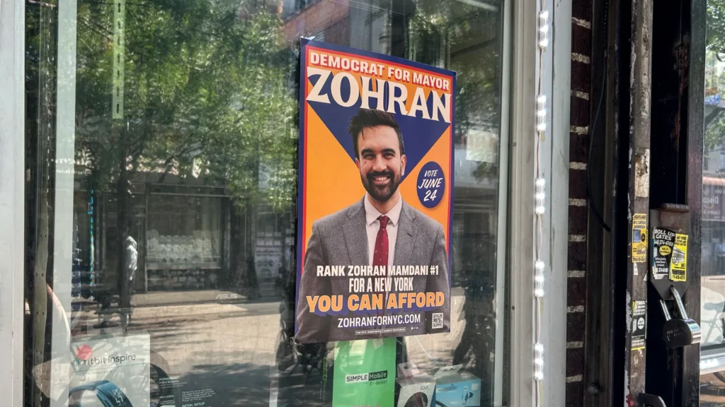 A poster for mayoral candidate Zohran Mamdani hangs on a storefront in Jackson Heights, Queens, New York City [Joanna Insco/ Al Jazeera]