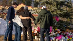 Residents hug as they place flowers at a memorial for the victims of Tuesday’s mass shooting in Tumbler Ridge, British Columbia, Canada, on Thursday, Feb. 12, 2026. (Christinne Muschi/The Canadian Press via AP)