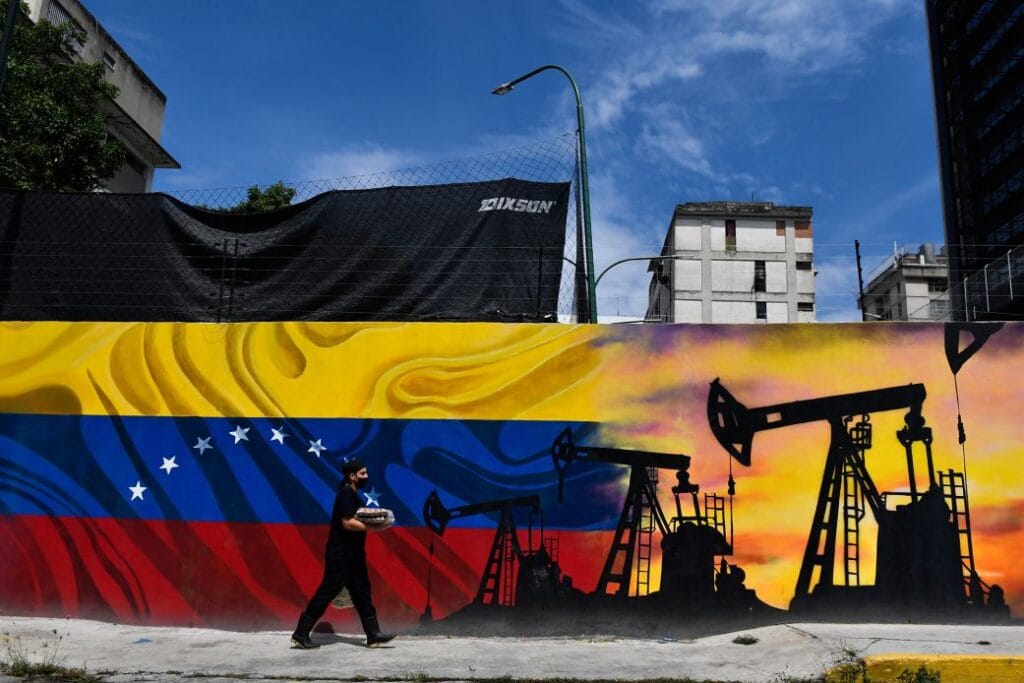 US Grants Two Licences Allowing Oil Majors to Restart Operations in Venezuela A man wearing a face masks walks past a mural depicting an oil pump and the Venezuelan flag in a Caracas street on May 26, 2022. (Federico Parra/AFP/Getty Images)