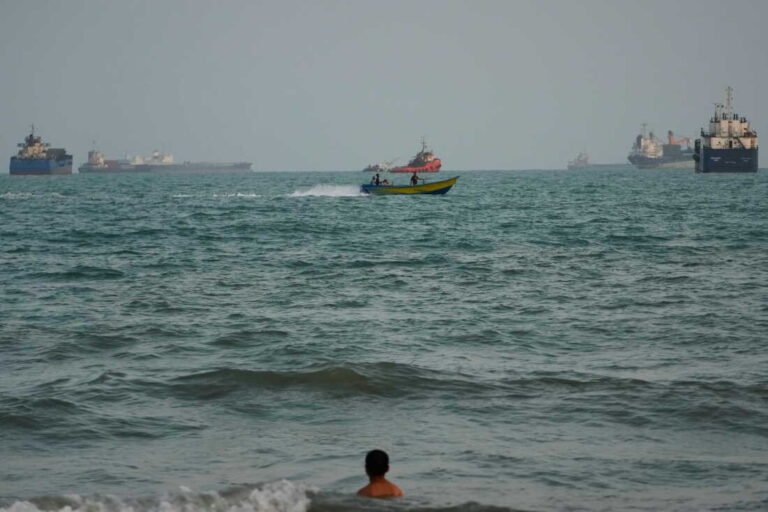 A swimmer remains near the shore as a motorboat passes commercial vessels anchored in the Strait of Hormuz off Bandar Abbas, Iran, on Friday. (Vahid Salemi/AP)